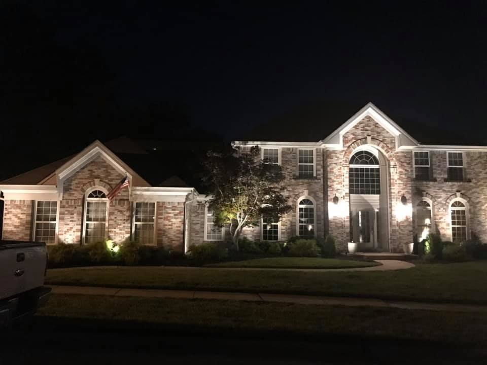 Lit brick suburban house at night with bright exterior lights and dark sky