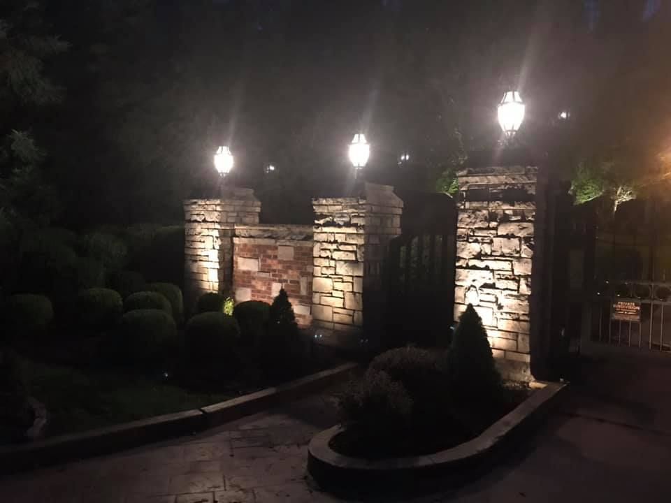 Illuminated stone gate pillars and landscaped entrance at night with small lights and shrubs