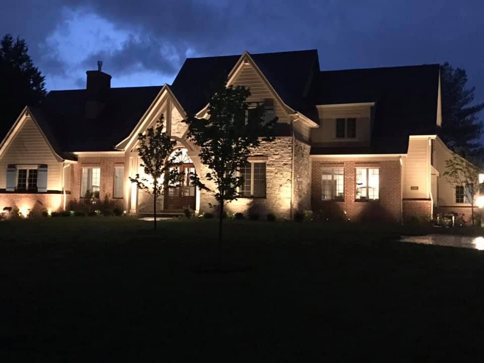 Warmly lit house and garden at night with glowing pathway lights and trees