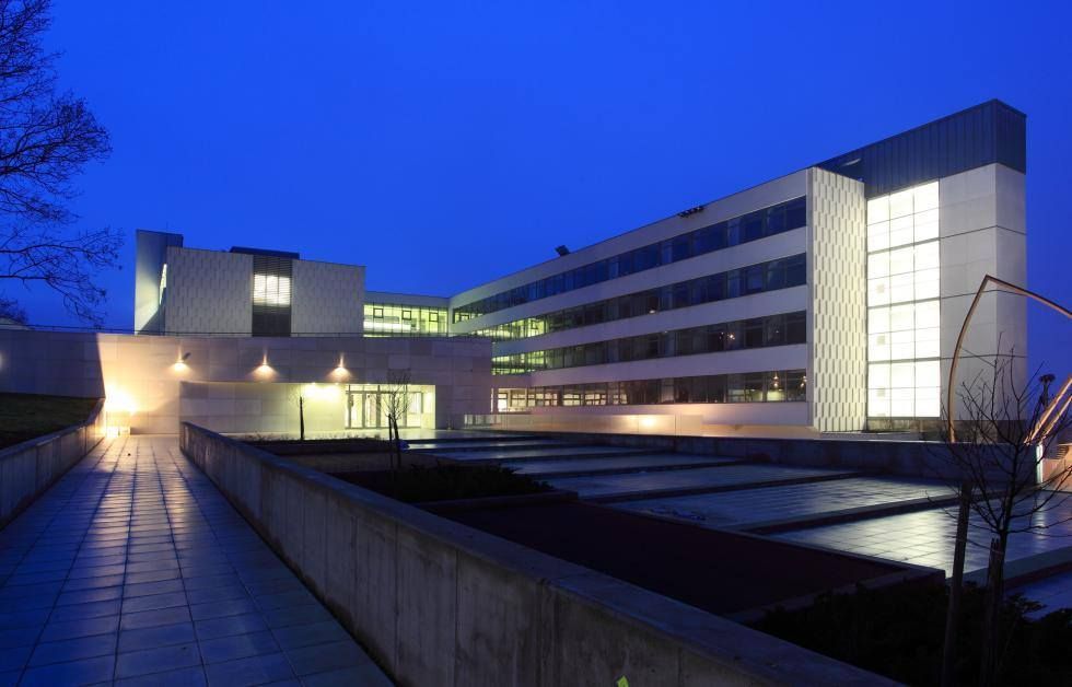 Modern building at dusk with blue-lit exterior and illuminated windows beside a walkway