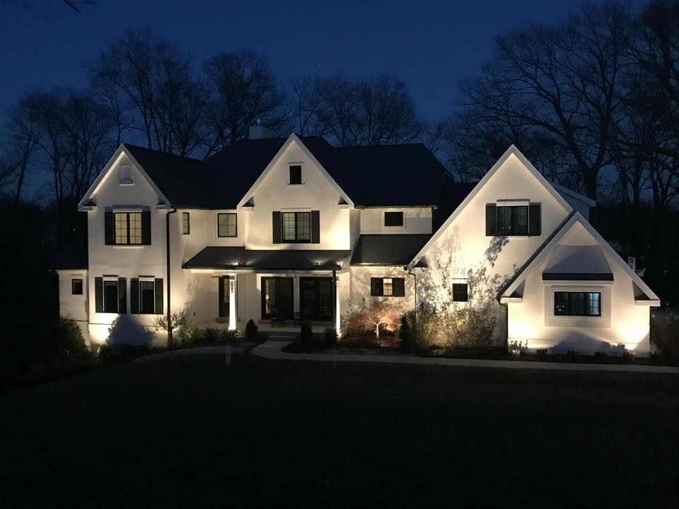 Large white house lit at night with dark roof and trees silhouetted against a blue sky