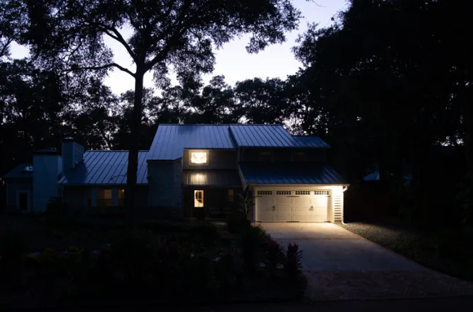 Brick house at night with warm exterior lights and dark trees silhouetted against the sky