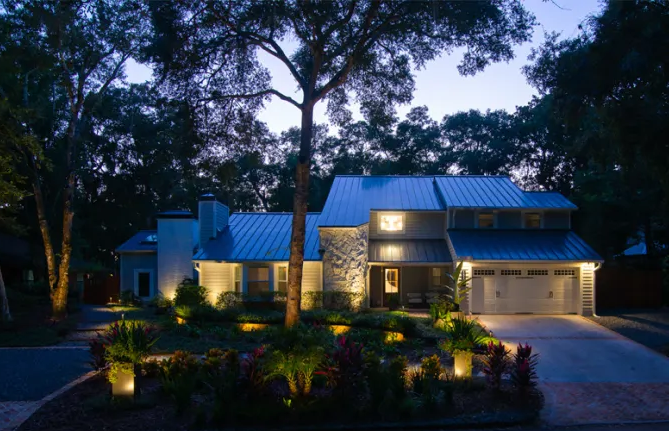 Warmly lit brick house at night with landscaped front yard and dark blue sky