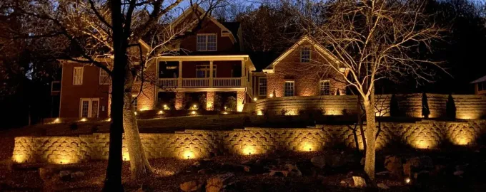 Nighttime view of a warmly lit house with stone walls and trees reflected in water