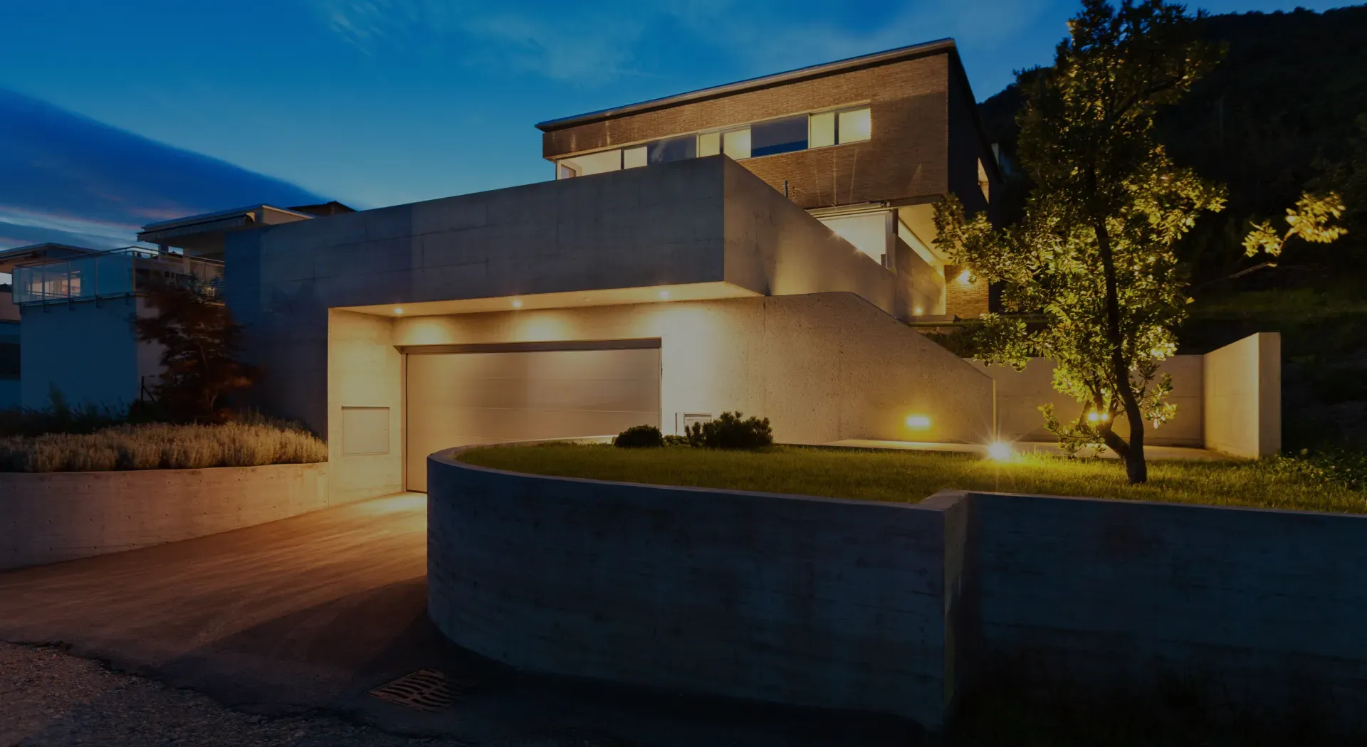 Modern two-story house at dusk with warm exterior lights and a curved front wall