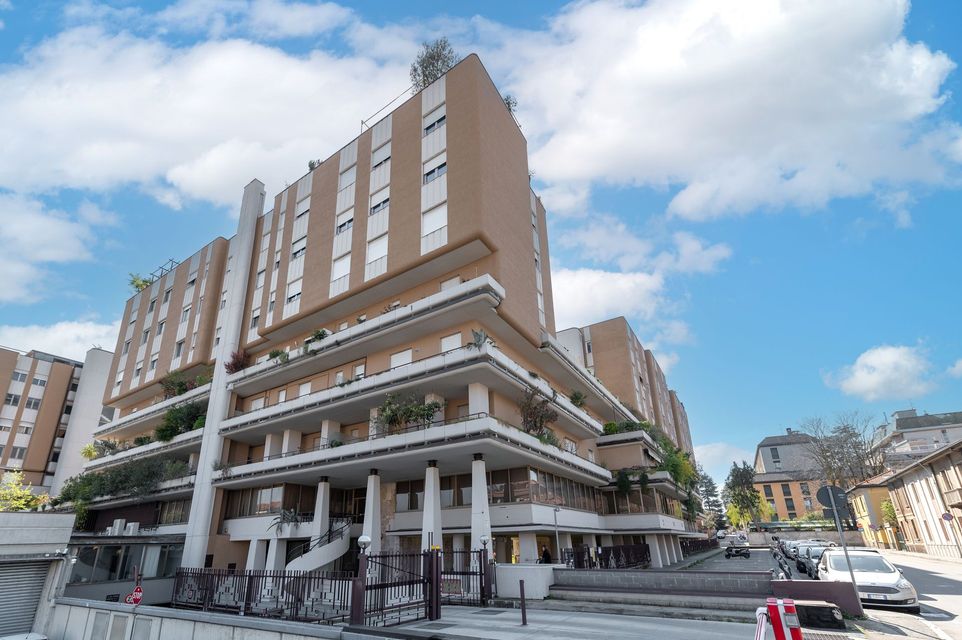 Moderno edificio a più piani con balconi, facciata beige e cielo azzurro.