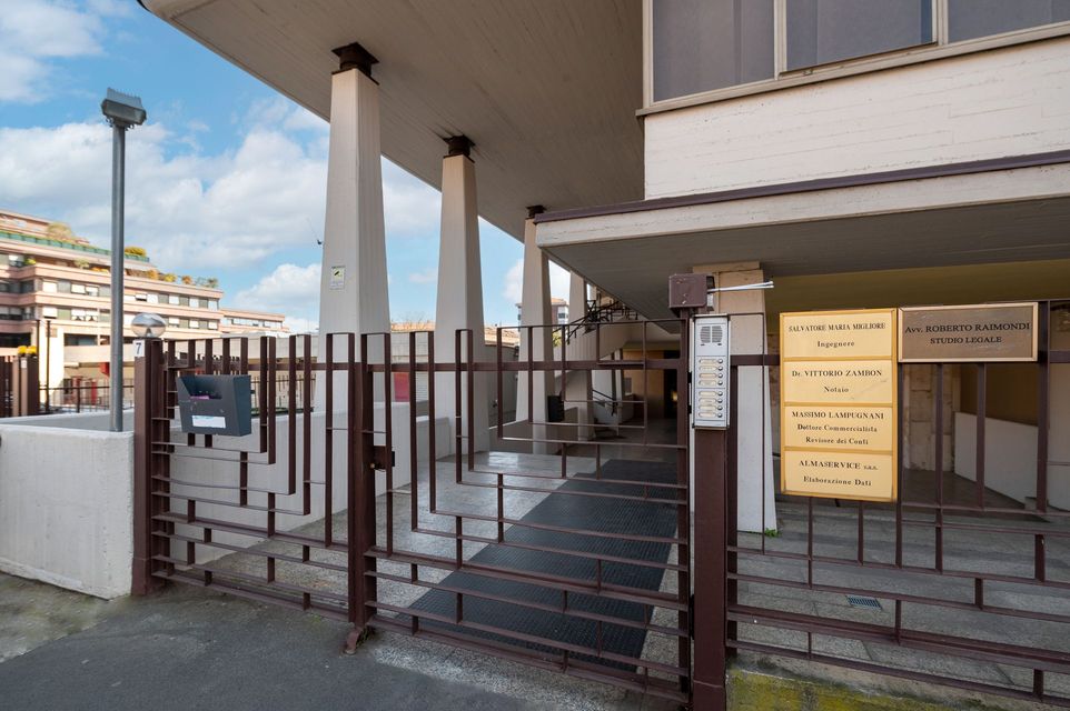 Esterno di un edificio con colonne e ingresso con cancello. Sono visibili due cartelli.