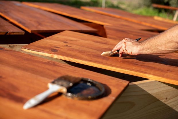 Person applying stain to several wooden boards outdoors. Person applying stain to several wooden boards outdoors.