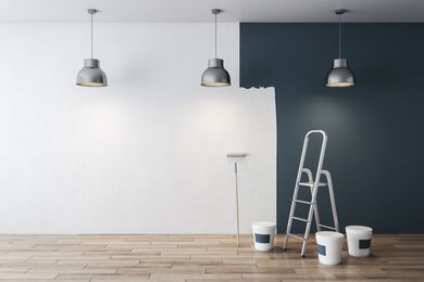 A room being painted with a white wall and a dark blue wall. A ladder, paint buckets, and a roller are present. A room being painted with a white wall and a dark blue wall. A ladder, paint buckets, and a roller are present.
