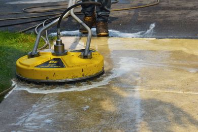 Person using a yellow surface cleaner to wash a concrete driveway. Person using a yellow surface cleaner to wash a concrete driveway.