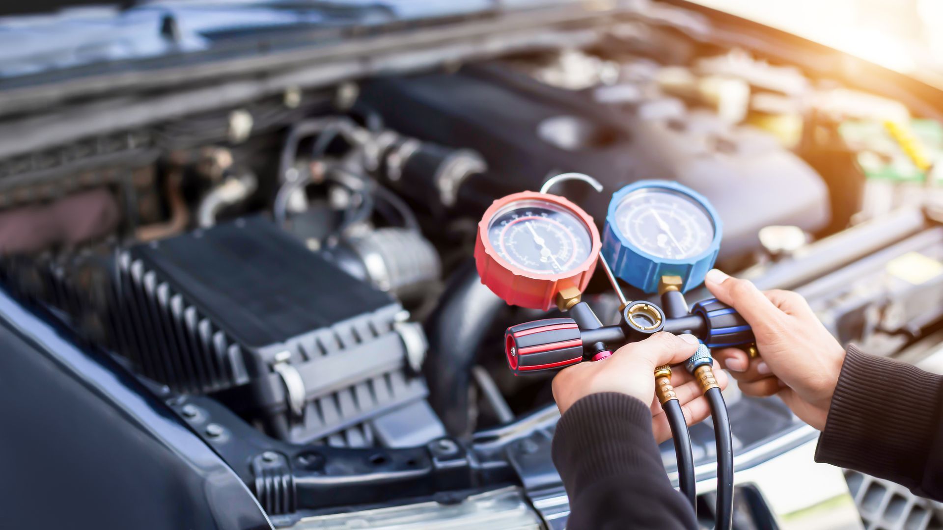 A person is holding two gauges in front of a car engine.