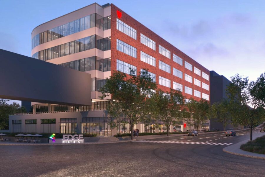 Office building with brick facade, arched windows, pedestrian bridge, trees, and signage.