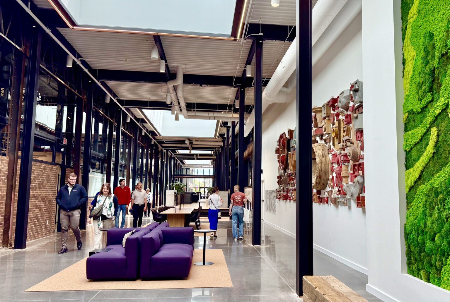 People walking down a long hallway with art and a living wall. Modern building with purple seating.