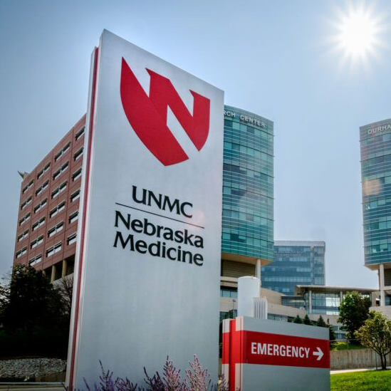 Sign for UNMC Nebraska Medicine, red logo with buildings and sunny sky.
