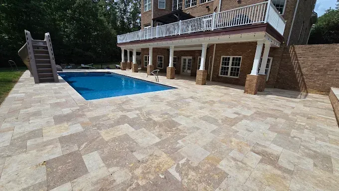 Backyard with pool, stone patio, and a two-story brick house with balcony.