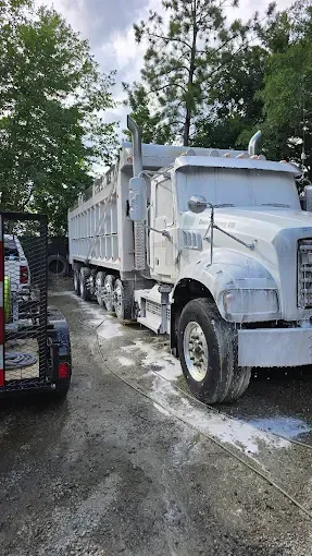 White dump truck parked on a gravel surface next to a forklift. Trees in the background.