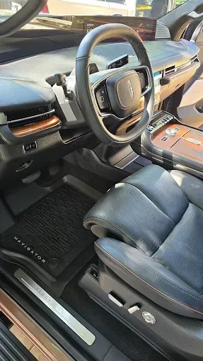 Interior of a Lincoln Navigator, showing steering wheel, leather seats, wood trim, and floor mats.