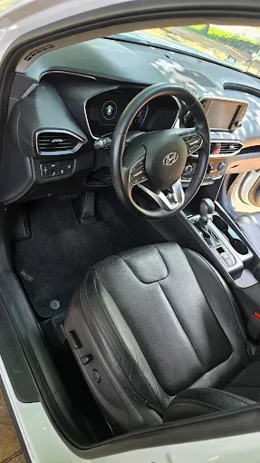 Interior view of a modern car's driver's seat. Black leather seat, steering wheel, dashboard, and carpet.