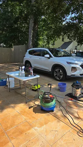 White SUV being detailed outdoors with a table of cleaning supplies and various equipment.