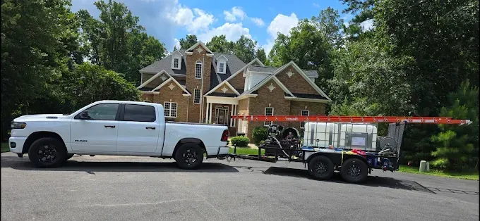 White pickup truck towing a trailer with water tanks parked in front of a brick house.