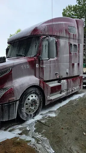 Red semi-truck covered in white foam suds, parked on a gravel shoulder.