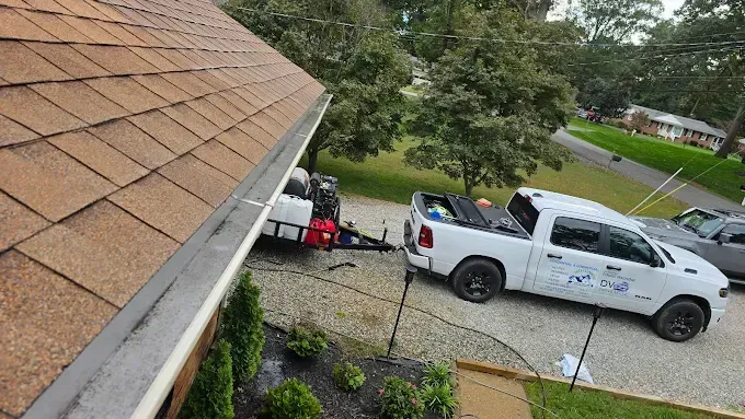 White truck and trailer parked on a driveway near a house; gutter cleaning setup.