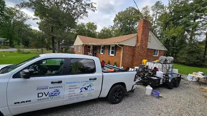 White truck with trailer parked in front of a brick house; pressure washing equipment visible.