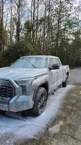 White foam covers a gray Toyota Tundra truck, being washed outside.