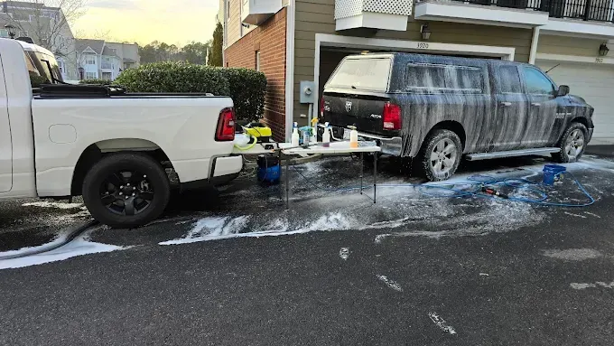 Truck washing a large SUV in a driveway, surrounded by suds and cleaning supplies.