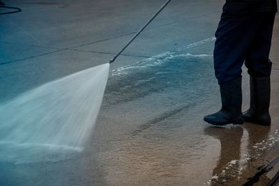 Person in boots power washing a wet concrete surface.