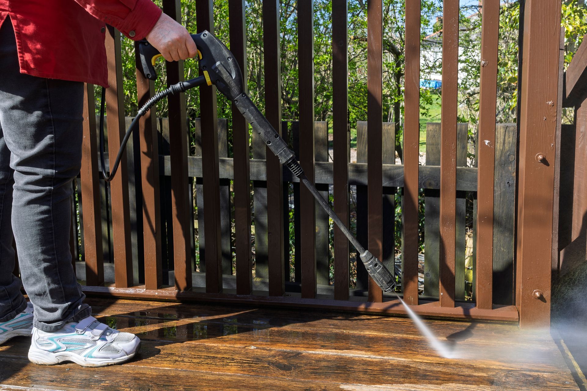 Person pressure washing a wooden deck with a high-pressure washer outdoors.