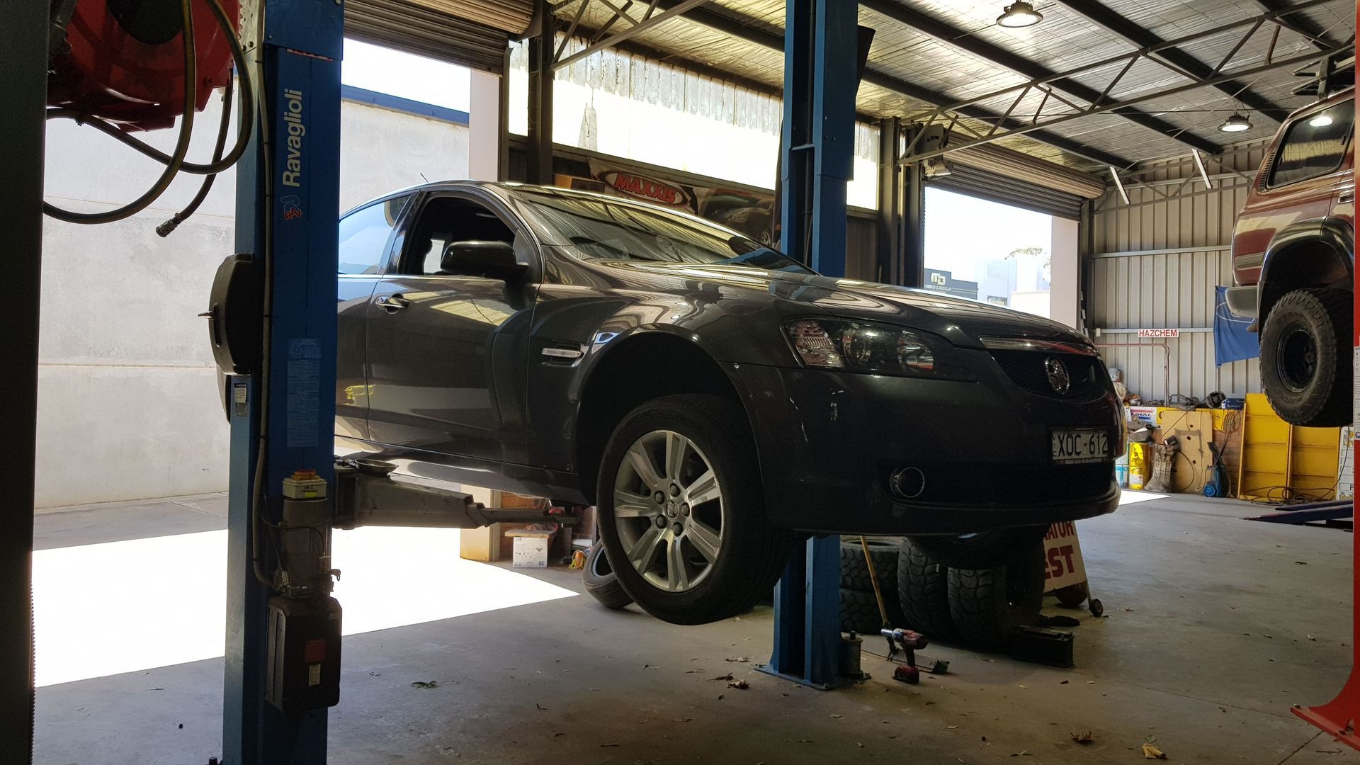 A dark gray car is raised on a lift inside a mechanic's garage.