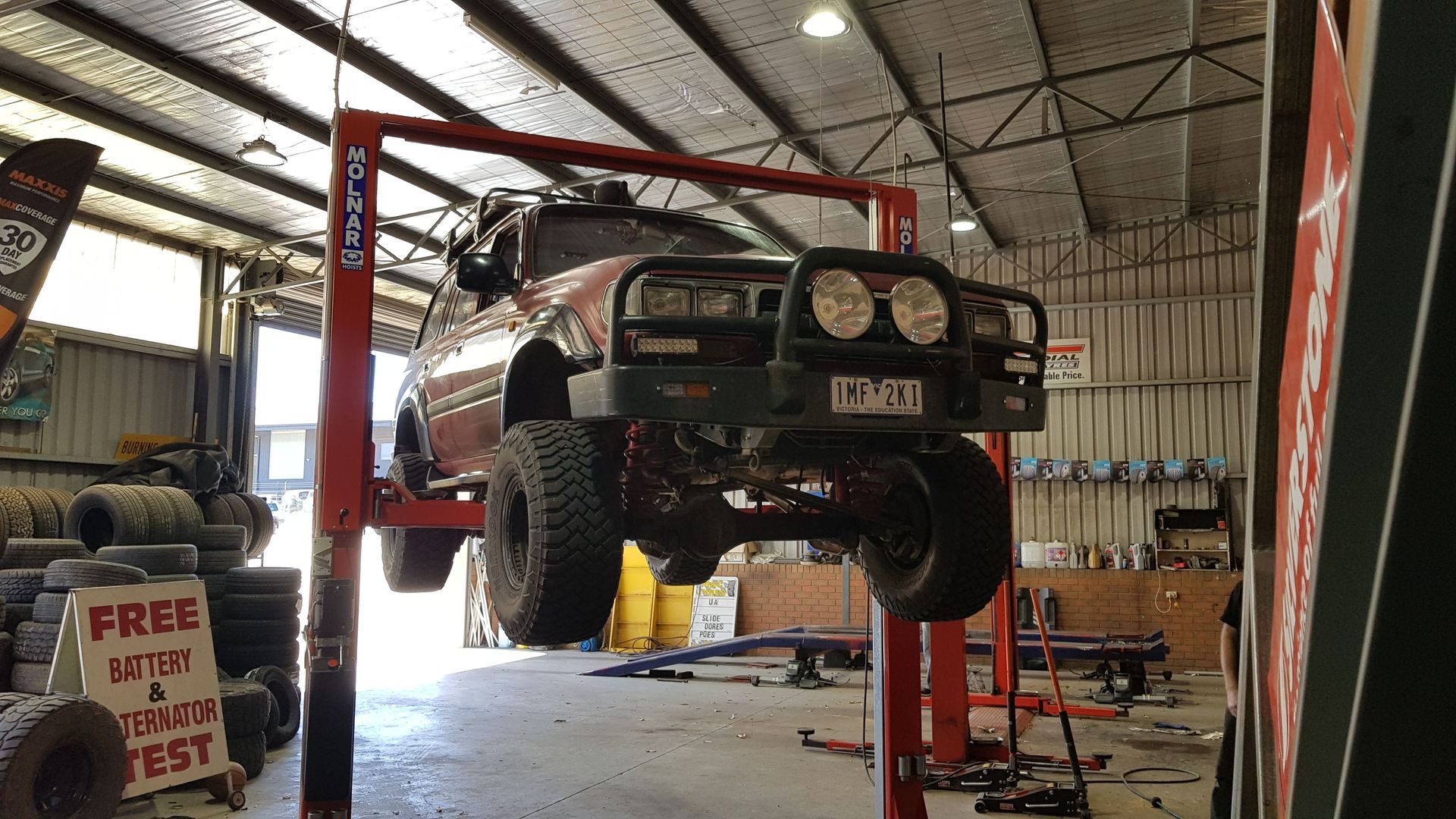 Off-road vehicle on a red lift in a garage with tires and tools visible.