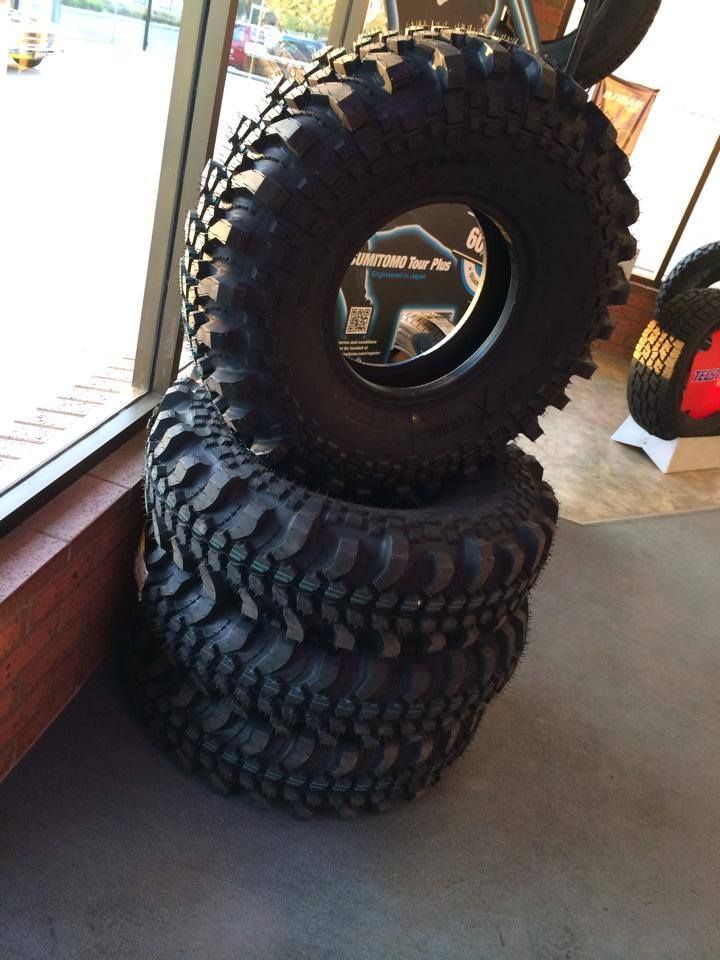 Four stacked black off-road tires, near a window, with a view of an interior.