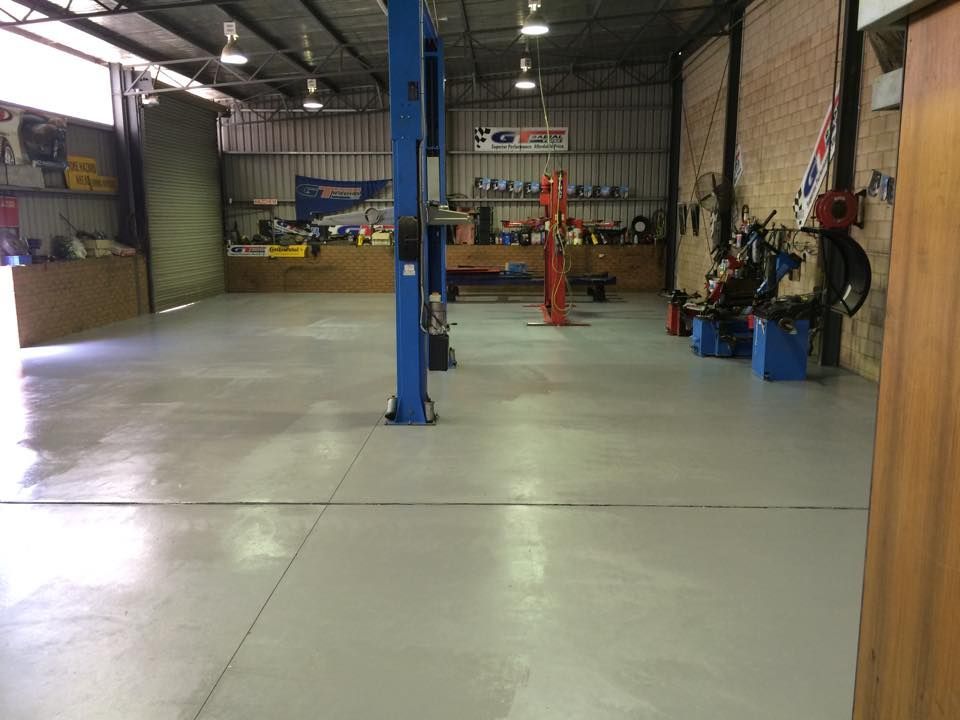 Wide view of an auto repair shop with a gray floor, tools, and a car lift.