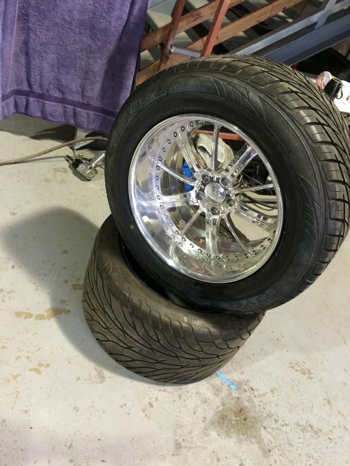 Two car tires, one chrome rimmed, stacked on a garage floor.