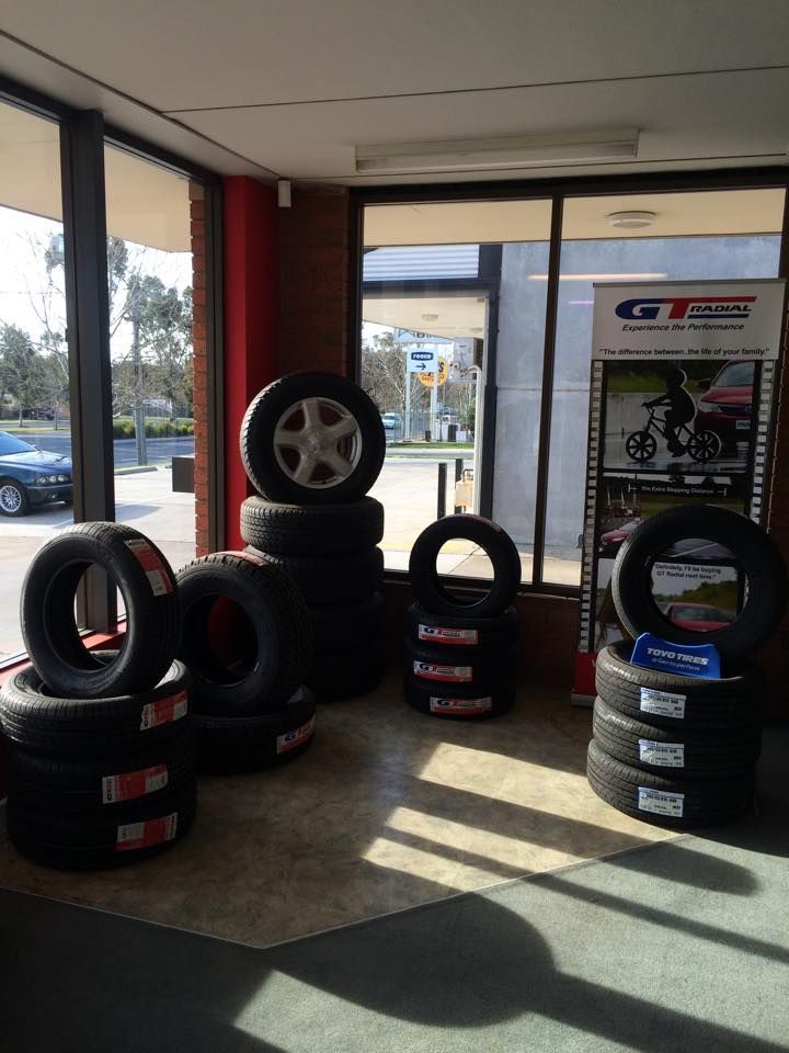 Tires stacked in a tire shop with a window view of outside, sunny day.