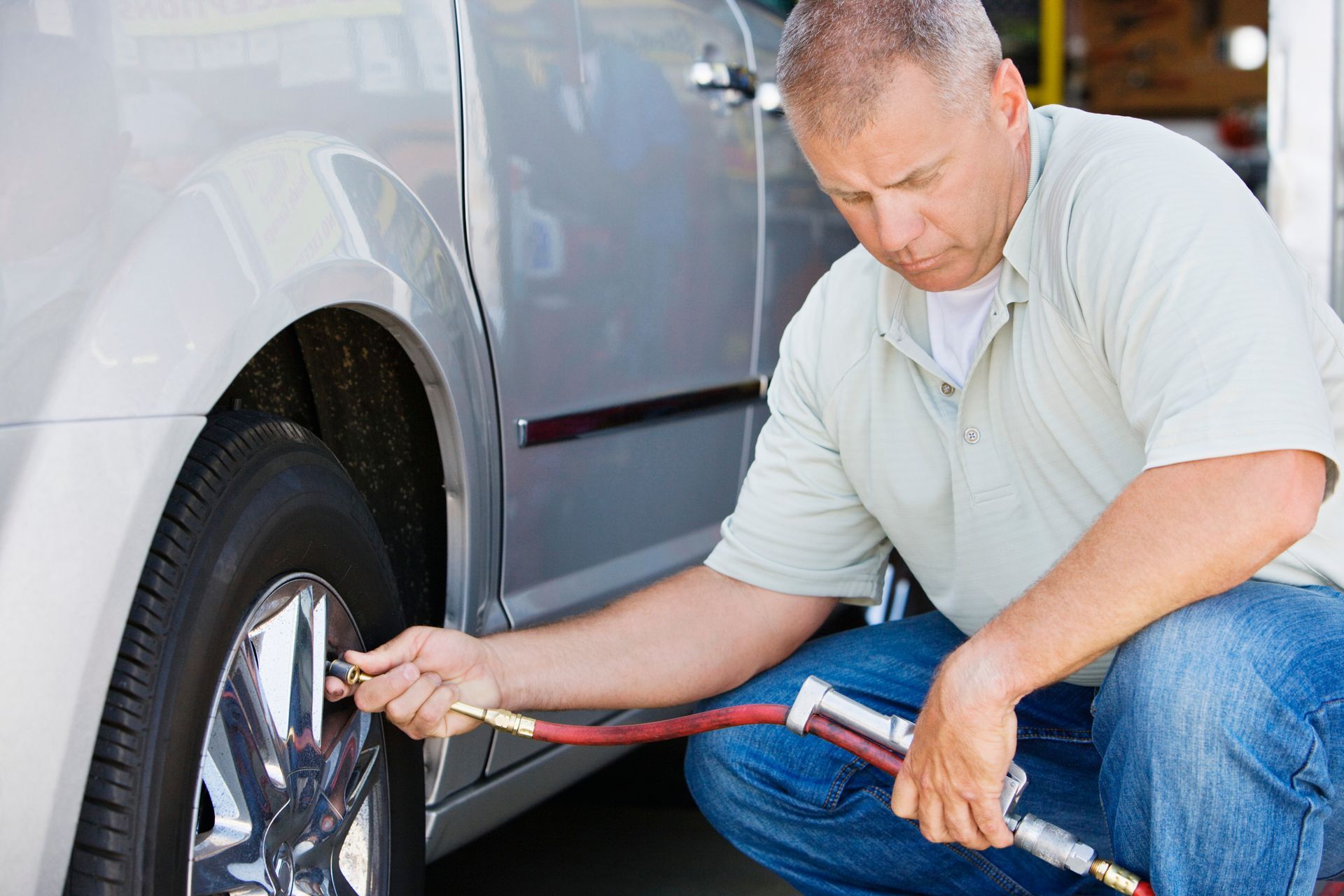 A mechanic kneels besides a car, using an air hose to inflate a flat tyre A mechanic kneels besides a car, using an air hose to inflate a flat tyre