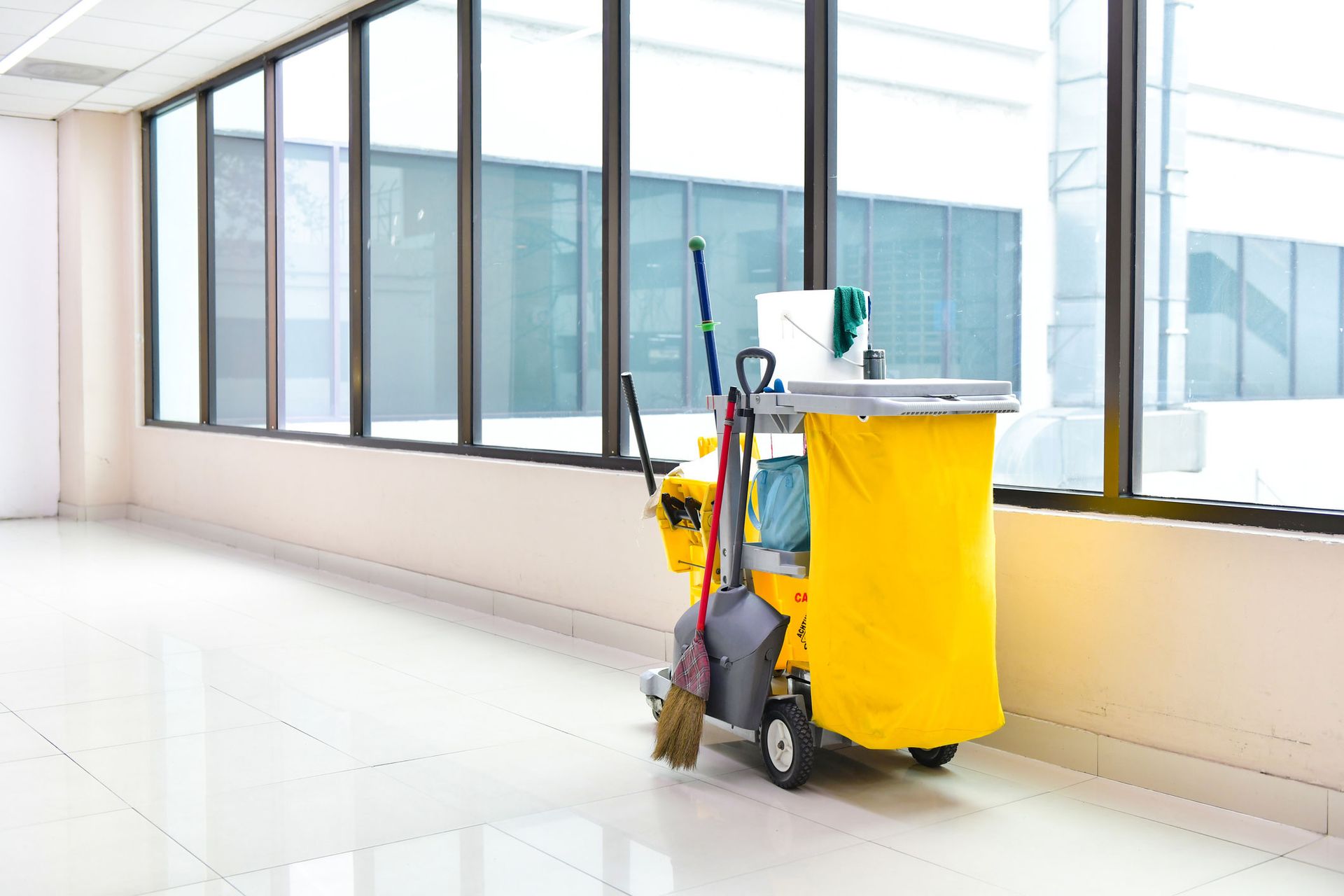 A yellow cleaning cart with a mop and broom in an empty room.