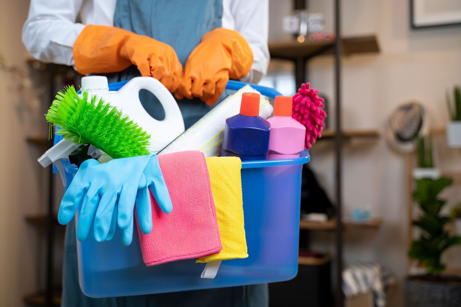 A person is holding a blue bucket filled with cleaning supplies.