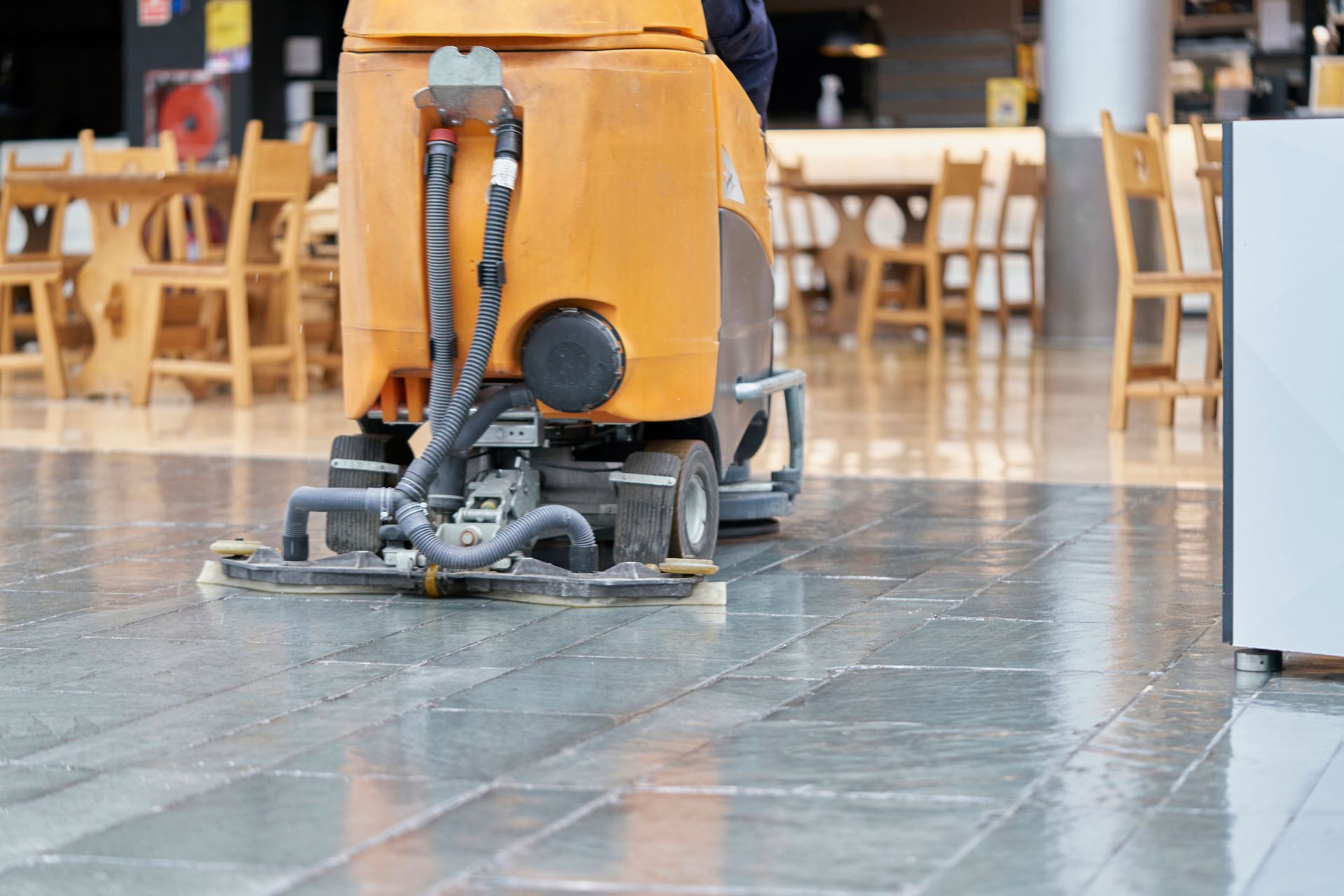A person is using a machine to clean a tiled floor in a restaurant.