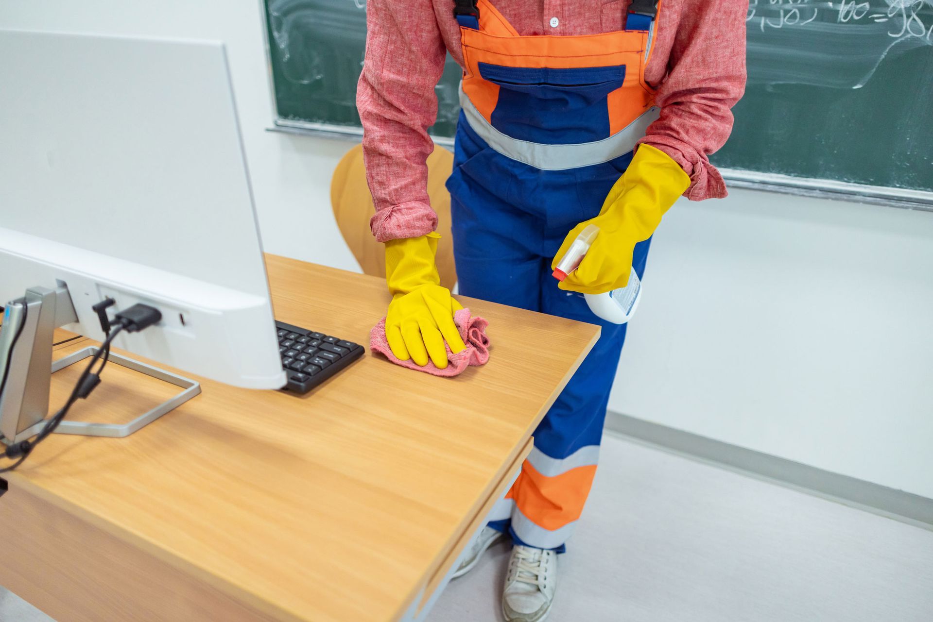 A person is cleaning a desk with a computer in a classroom.