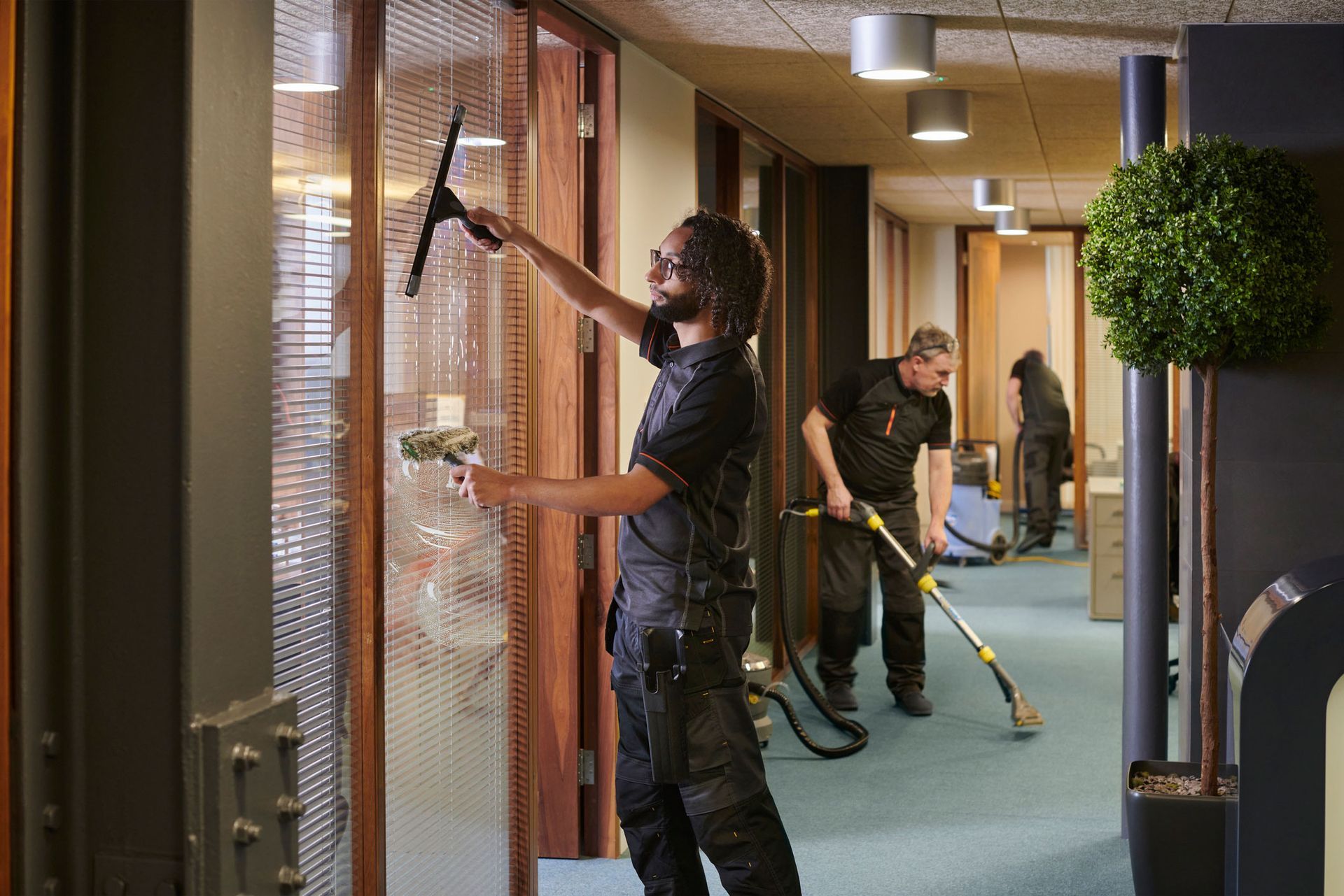 A man is cleaning a window with a squeegee in a hallway.