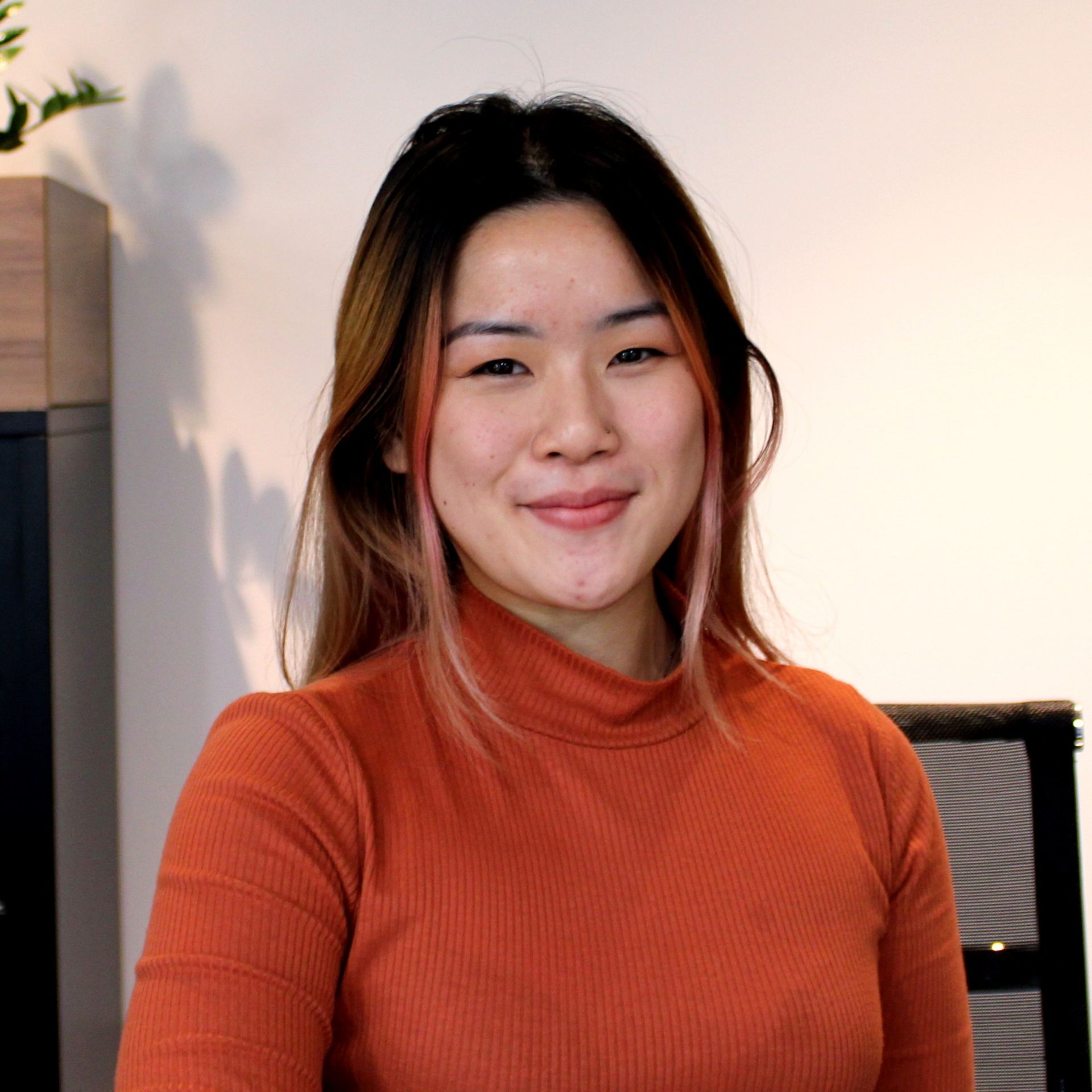 A woman in an orange sweater is smiling for the camera.