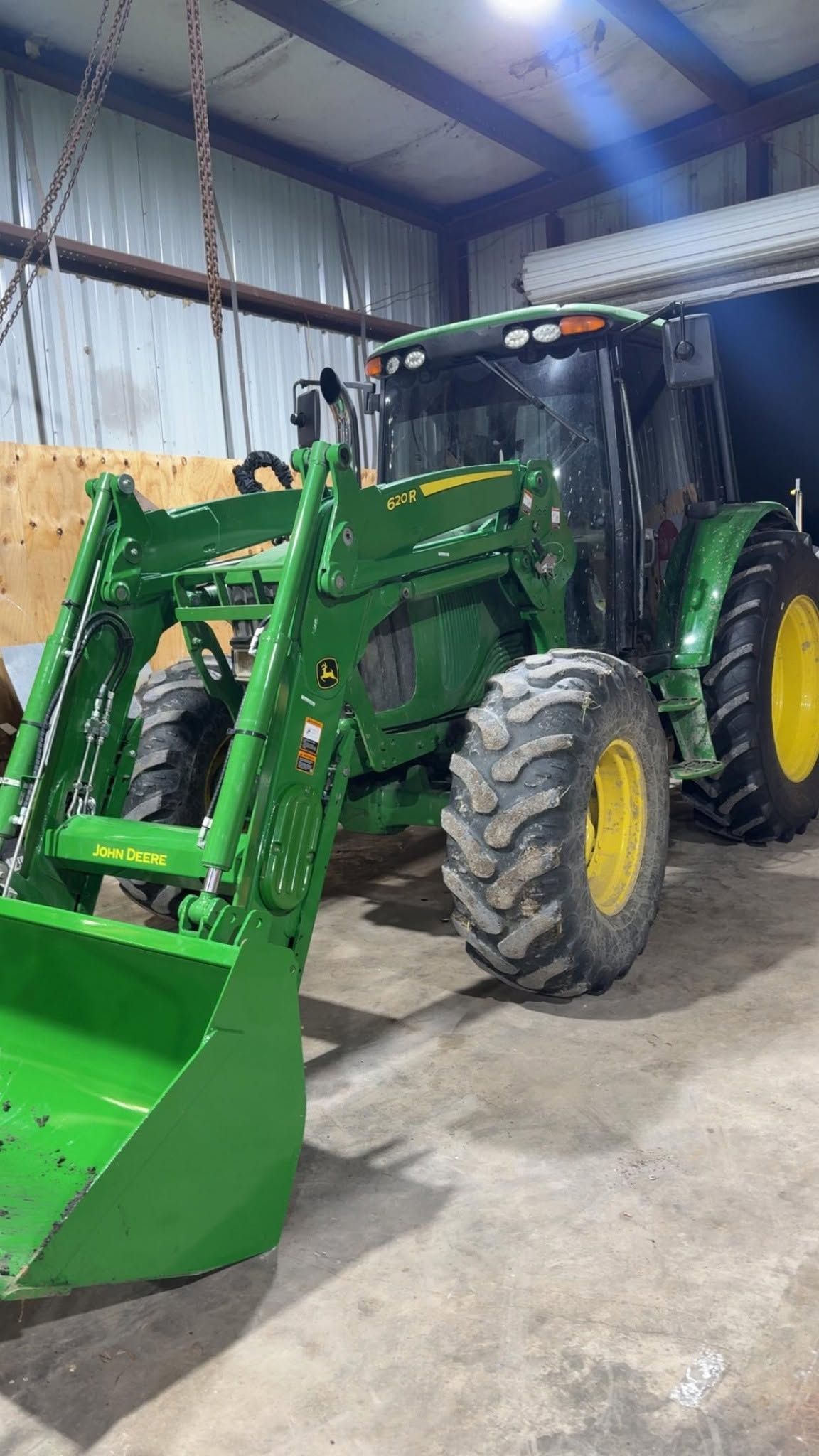Green tractor with front loader parked inside a garage or barn on a concrete floor.