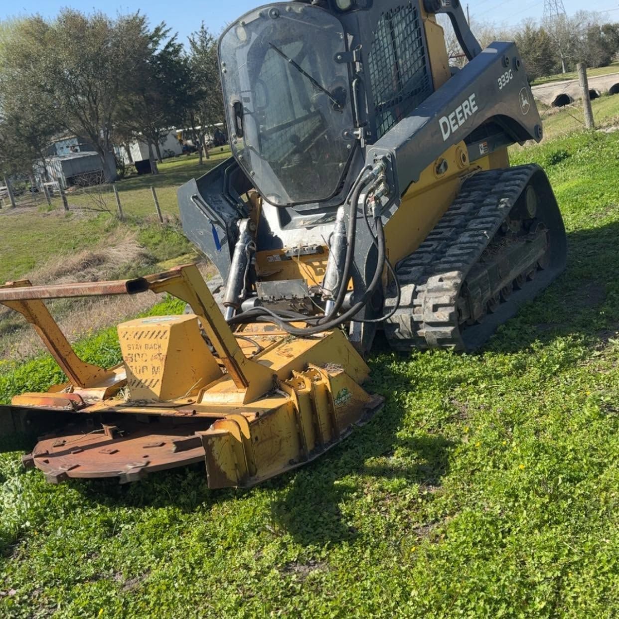 Black skid steer on grass with a yellow mower attachment in a rural field