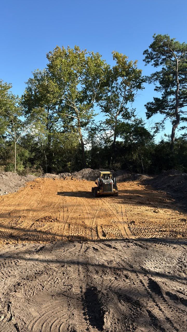 Small bulldozer leveling dirt on a cleared construction site bordered by trees under a blue sky