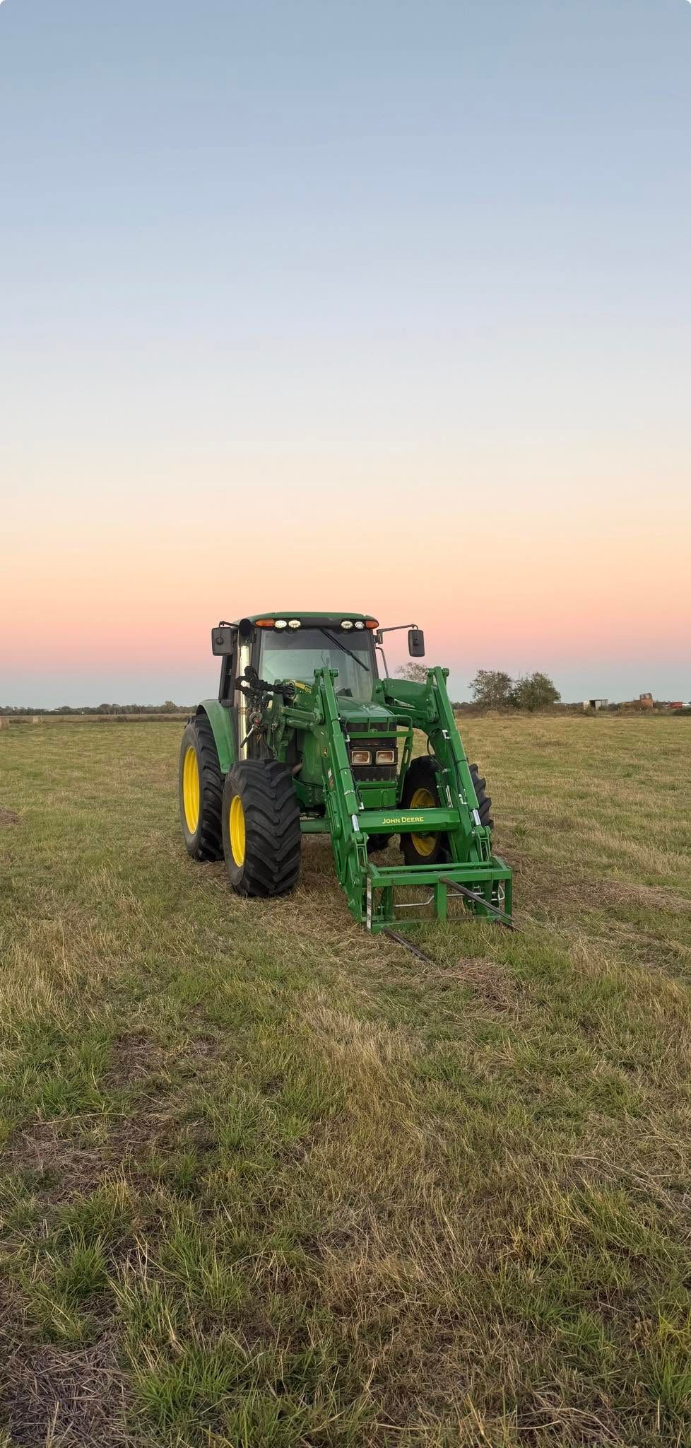 Green tractor in a harvested field at sunset under a pastel sky