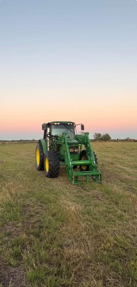 Green tractor in a grassy field at sunset, facing the camera.