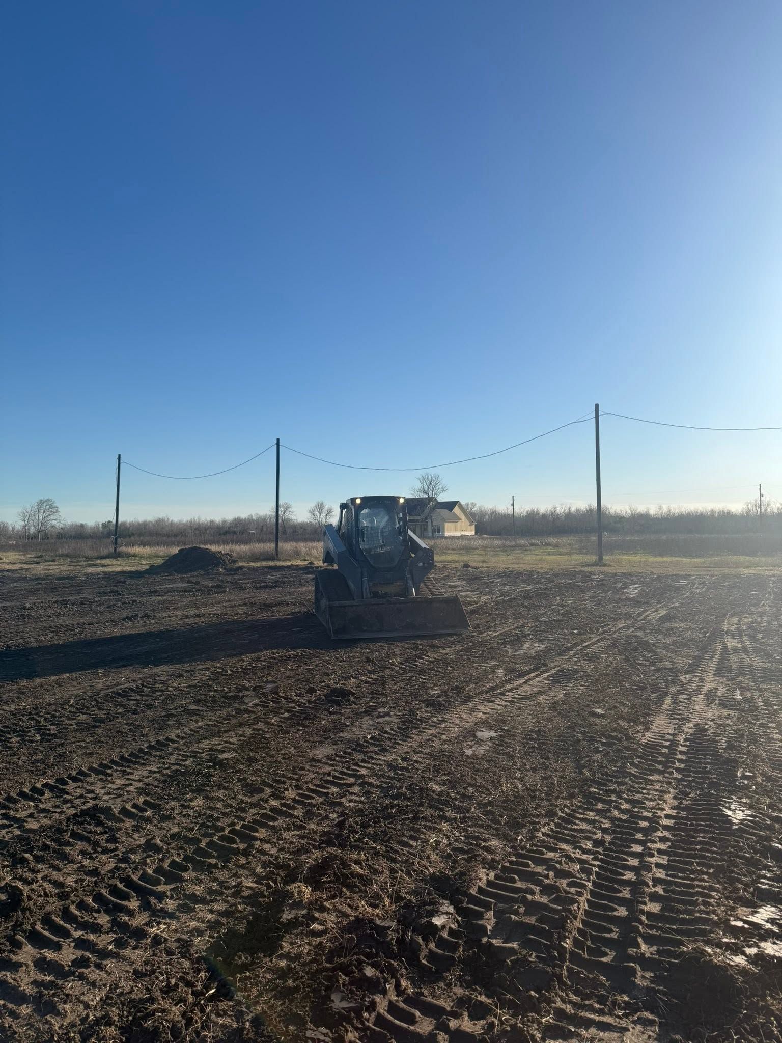 Tractor in a plowed field under a clear blue sky, with fence posts along the horizon.